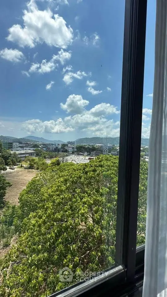 Stunning view from a window overlooking lush greenery and distant mountains under a clear blue sky.