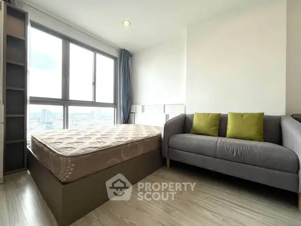 Modern bedroom with large window and cozy sofa, offering city views and natural light.