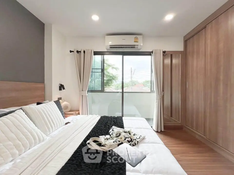 Modern bedroom with large window, wooden wardrobe, and cozy bedding in a stylish apartment.