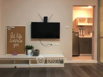 Modern living room with wall-mounted TV and open kitchen layout, featuring sleek cabinetry and contemporary decor.