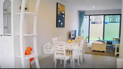 Charming dining area with elegant white furniture and natural light from large windows.