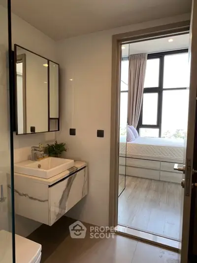 Modern bathroom with sleek design and view into a bright bedroom with large windows.