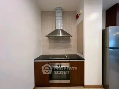 Modern kitchen with sleek oven and stovetop, featuring a stylish range hood and stainless steel fridge.