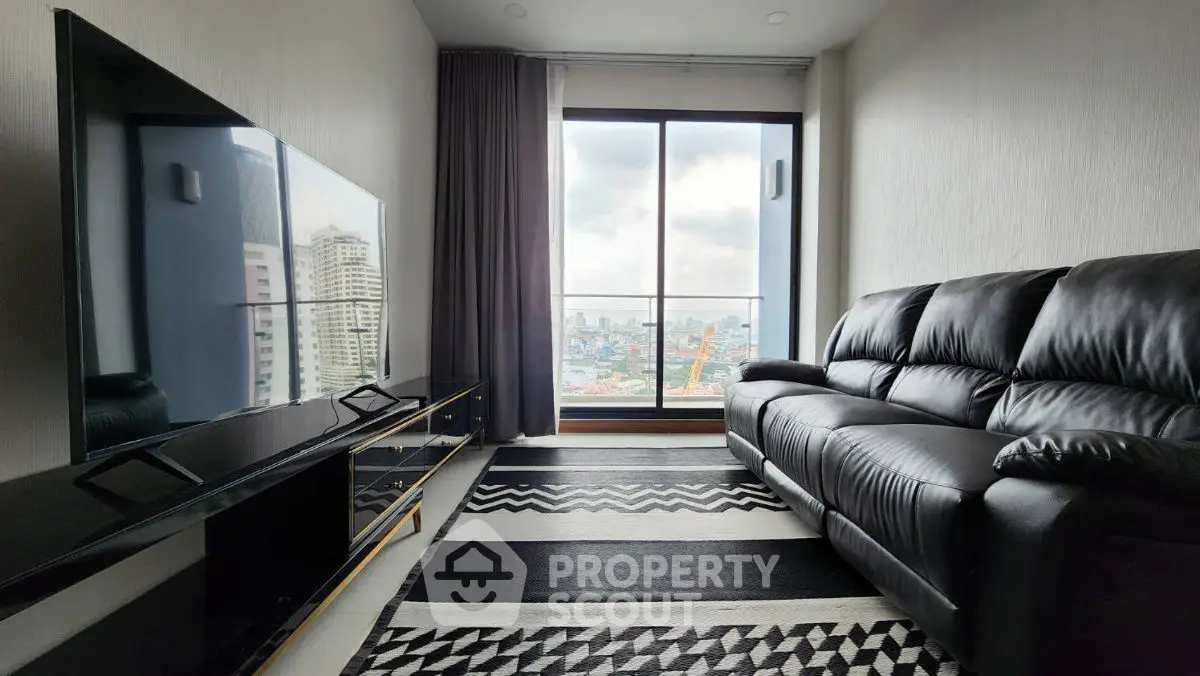 Modern living room with city view, sleek black leather sofa, and large flat-screen TV.