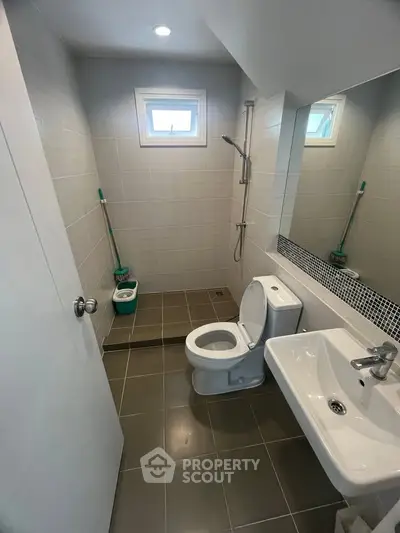 Modern bathroom with sleek fixtures and tiled walls, featuring a shower and a window for natural light.