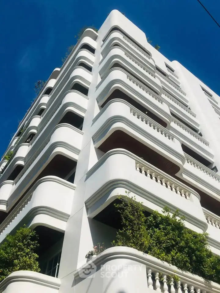Elegant white building with unique curved balconies and lush greenery against a clear blue sky.