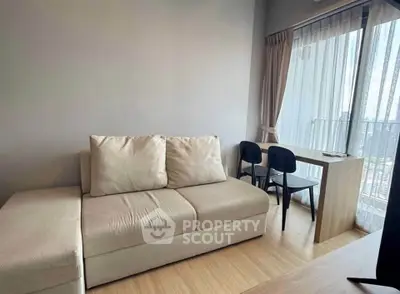 Modern living room with beige sofa and dining area near large window with city view.