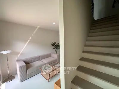 Modern living room with cozy sofa and stylish staircase in a bright, minimalist home.