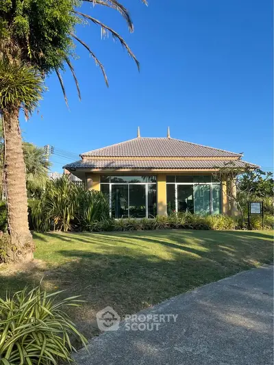 Charming single-story house with lush garden and palm trees under clear blue sky.