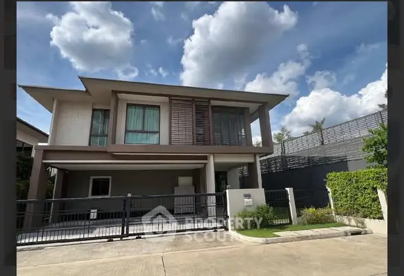 Modern two-story house with large windows and gated driveway under a clear blue sky.
