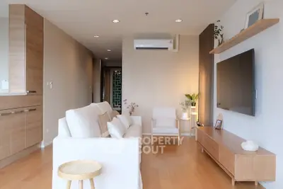 Modern living room with sleek furniture and wooden flooring, featuring a wall-mounted TV and air conditioning.