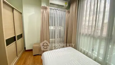 Cozy bedroom with natural light, featuring wooden floors and modern air conditioning.