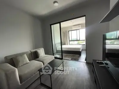 Modern living room with cozy sofa and view into a bright bedroom through glass doors.
