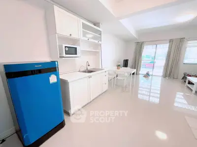 Modern open-layout kitchen with sleek white cabinets and blue fridge in bright living space.