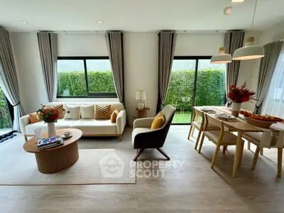 Modern living room with stylish decor and dining area, featuring large windows and natural light.