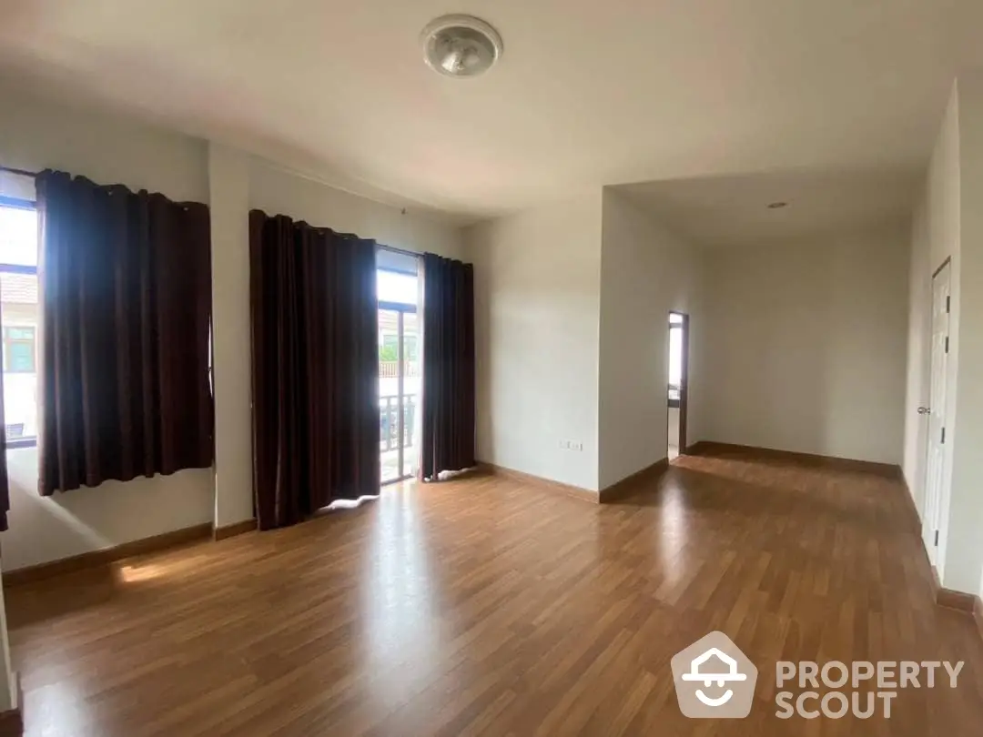 Spacious and sunlit living room with gleaming hardwood floors and large windows draped in elegant dark curtains, offering a blank canvas for personalized decor.