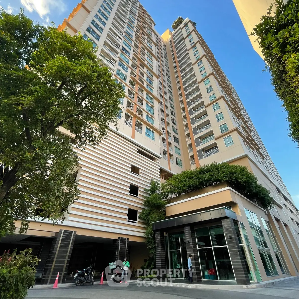 Modern high-rise building with lush greenery and glass facade under clear blue sky.