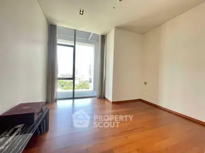 Spacious empty room with wooden flooring and large window offering city view.