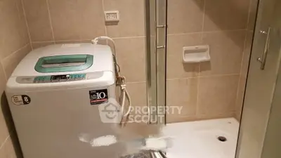 Compact bathroom with washing machine and shower enclosure in modern apartment.