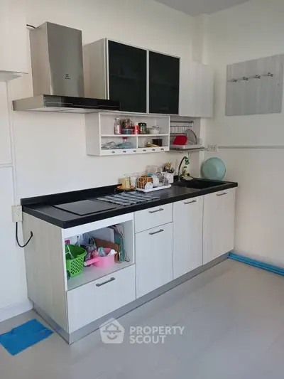 Modern kitchen with sleek cabinetry and black countertop, featuring open shelving and stainless steel appliances.
