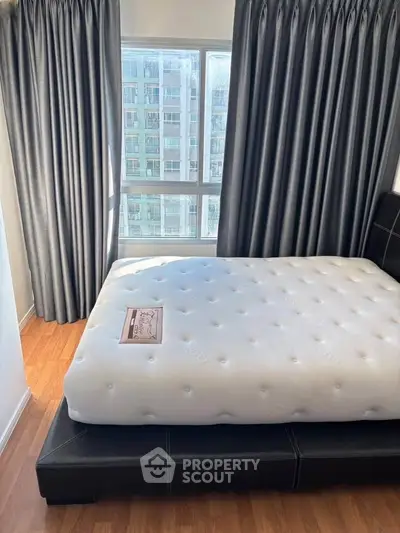 Spacious bedroom with large window and modern decor in urban apartment.