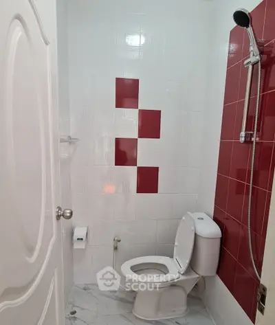 Modern bathroom with red and white tile design and shower setup.