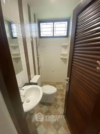 Compact bathroom with modern fixtures and natural light from window, featuring a shower and stylish tile flooring.