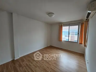 Spacious empty room with wooden flooring and large window, perfect for customization.