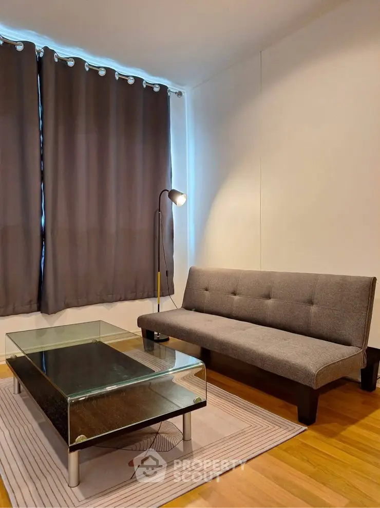 Modern living room with sleek sofa, glass coffee table, and elegant curtains.