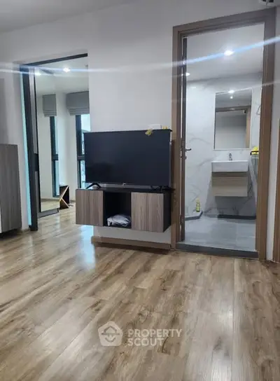 Modern living room with wooden flooring and TV unit, adjacent to a sleek bathroom.