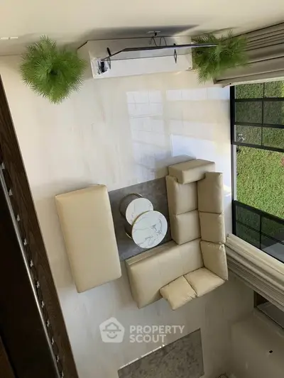 Spacious living room with modern beige sectional sofa and marble coffee tables, overlooking a lush garden.