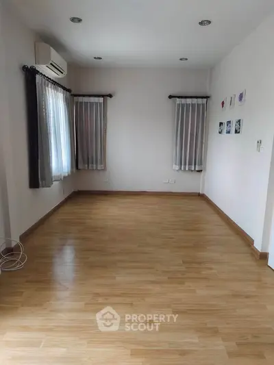 Spacious empty room with wooden flooring and large windows, perfect for customization.