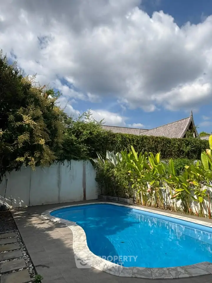 Stunning private pool with lush greenery and clear blue skies, perfect for relaxation and leisure.