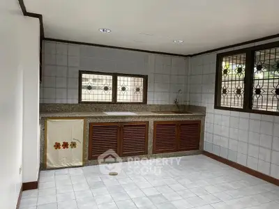 Spacious kitchen with tiled walls and wooden cabinets, featuring a large countertop and natural light.