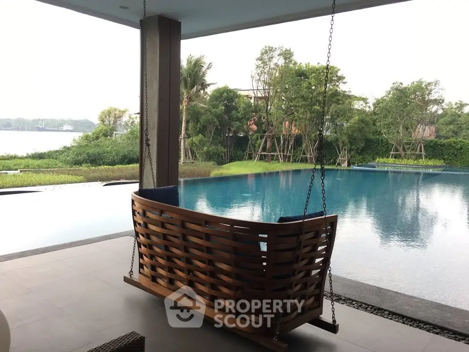 Luxurious poolside view with elegant wooden swing overlooking serene water and lush greenery.