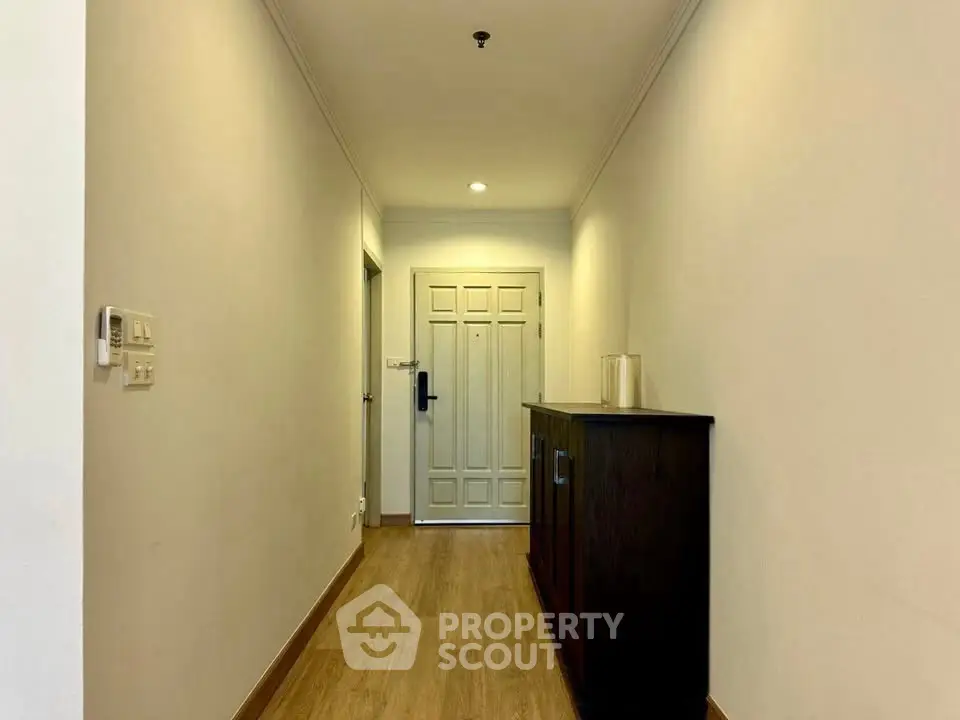 Spacious hallway with wooden flooring and elegant cabinetry leading to a classic white door.