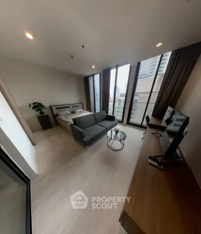 Modern bedroom with large windows and city view, featuring a cozy bed, stylish sofa, and sleek workspace.