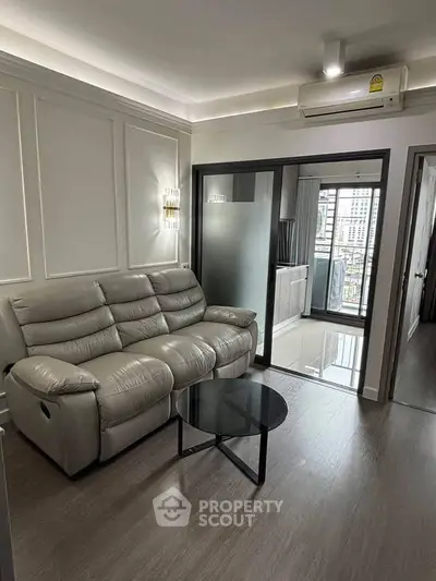 Modern living room with sleek leather sofa and glass door leading to balcony with city view.