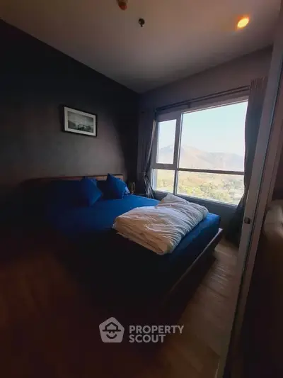 Cozy bedroom with scenic mountain view from large window, featuring a comfortable bed and stylish decor.