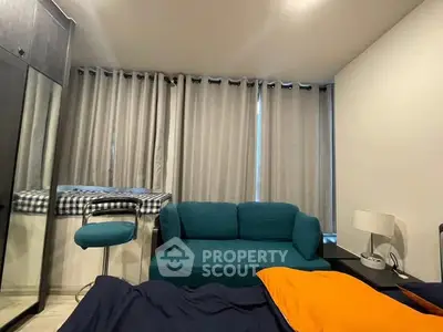 Cozy bedroom with modern decor, featuring a teal sofa, stylish curtains, and a sleek bedside lamp.