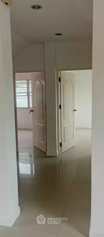 Spacious hallway with glossy tiled floors and open doors leading to bright rooms.
