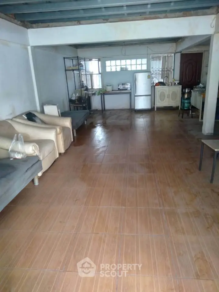 Spacious open-plan living area with tiled flooring and basic furnishings.