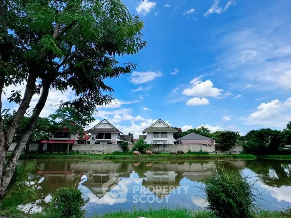 Charming riverside homes with lush greenery and serene water reflections under a vibrant blue sky.