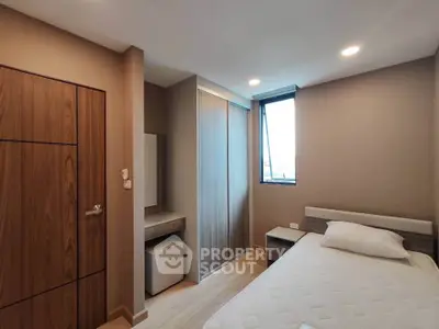 Modern bedroom with sleek design, featuring a comfortable bed, built-in wardrobe, and natural light from a large window.