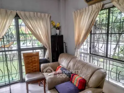 Cozy living room with large windows and garden view, featuring comfortable seating and elegant curtains.