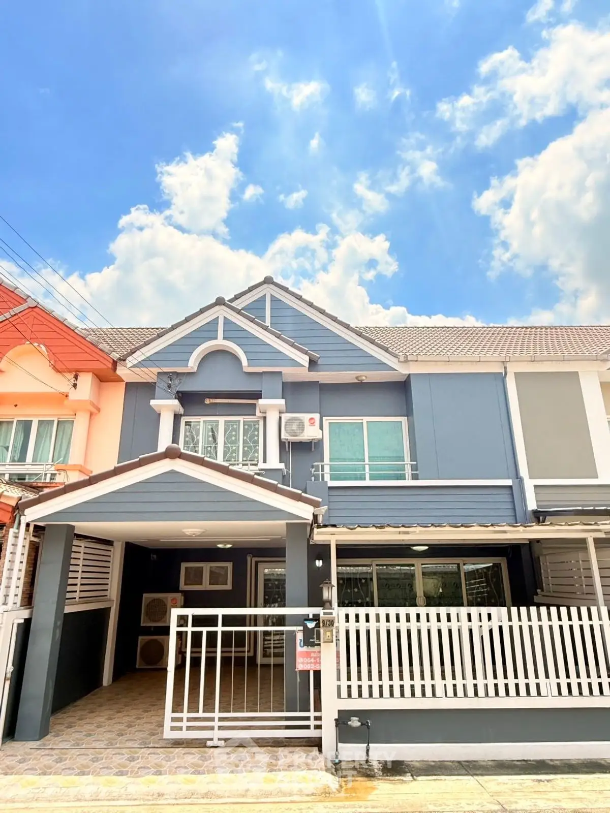 Charming townhouse with modern facade and gated entrance under a bright blue sky.