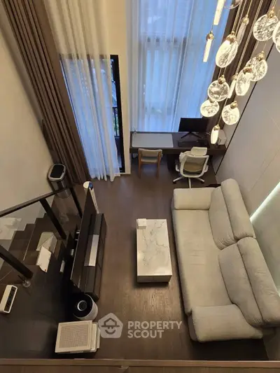 Modern living room with high ceiling, elegant chandelier, and cozy seating area.