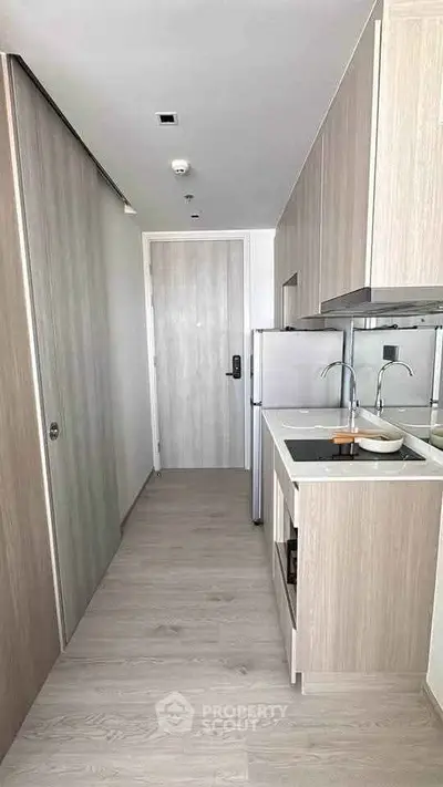 Modern compact kitchen with sleek wooden cabinetry and built-in appliances in a stylish apartment.