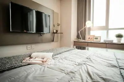 Cozy bedroom with a large comfortable bed, wall-mounted TV, and ample natural light streaming through the window, perfect for relaxation.