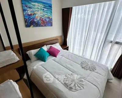 Cozy bedroom with modern decor and large window, featuring colorful pillows and abstract art.